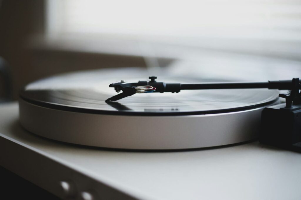 Close up of a turntable tonearm resting on a spinning vinyl record in soft natural light