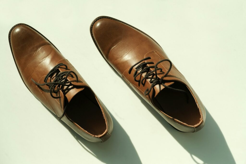 A pair of brown leather lace-up derby shoes seen from above on a pale background